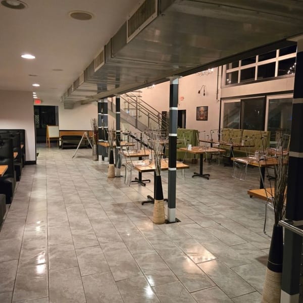 Empty restaurant dining room with tiled floors, booths, tables with clear chairs, and a staircase.