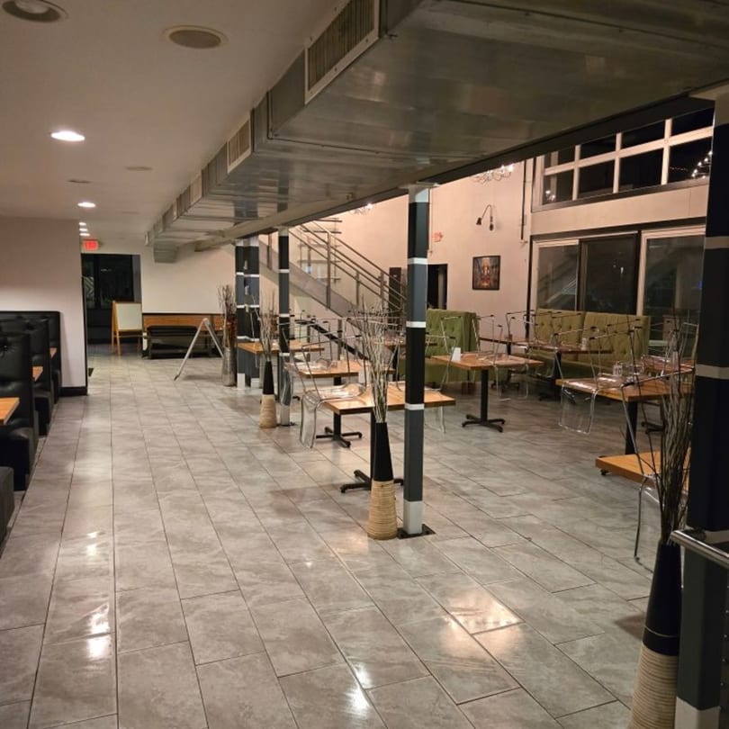 Empty restaurant dining room with tiled floors, booths, tables with clear chairs, and a staircase.