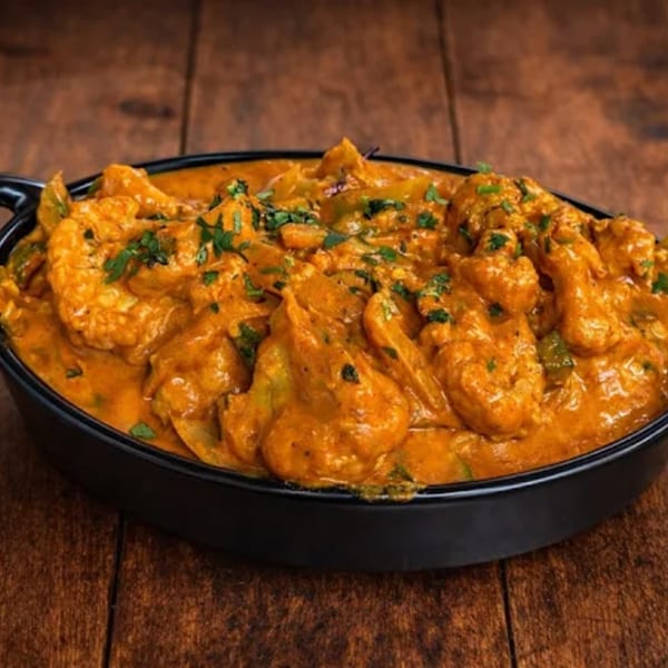 A black bowl filled with creamy orange curry, garnished with fresh green herbs, on a wooden table.