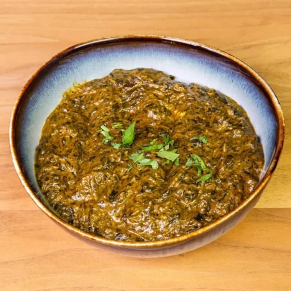 A bowl of vibrant green saag, an Indian spinach dish, garnished with fresh herbs.
